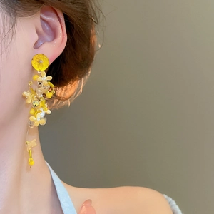 Detail of yellow flower tassel earrings featuring bead accents on female model