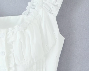 Detailed close-up of white eyelet embroidery and ruffle trim with white buttons