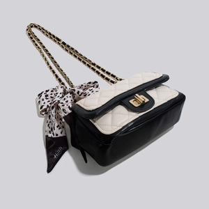 Détail d'un sac bandoulière matelassé noir et blanc avec chaîne dorée et foulard léopard