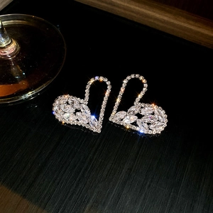 Macro shot of silver hollow heart earrings with brilliant zircon stones on dark surface