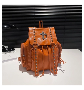 Macro detail of orange leather backpack featuring metal rivets and silver cross charm
