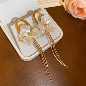 Detail of floral earrings with white petals, golden center, and long chain tassels