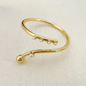 Detail of a spiral gold-plated brass cuff bracelet featuring elegant pearls and gold beads