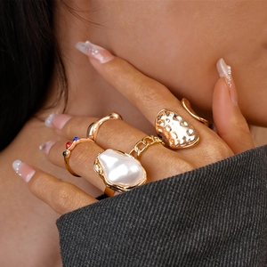 Close-up of stacked gold geometric rings with pearls and rhinestones on fingers