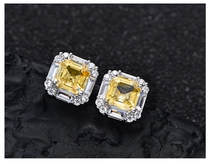Macro view of square yellow diamond earrings on dark stone highlighting detailed halo craft