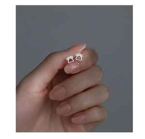 Macro shot of silver cat paw stud earrings with cubic zirconia held by fingers