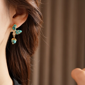 Gros plan d'une boucle d'oreille papillon en turquoise et or avec pendentif gland