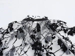 Close-up of black floral flocking on semi-transparent white mesh lace shirt