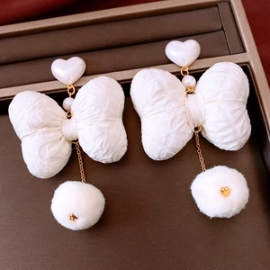 Detail of elegant white heart earrings with large fabric bows and plush fur pompom drops