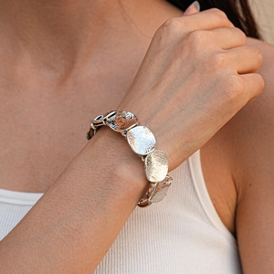 Dettaglio di bracciale in metallo argento con texture martellata su polso femminile