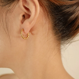 Close-up of golden twisted rope hoop earring worn by a model for minimalist style