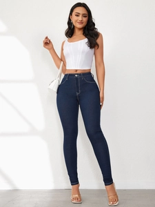 Detail of high waisted skinny blue jeans paired with white crop top and handbag