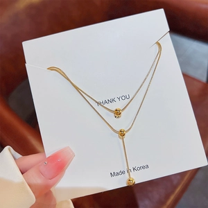 Double-layered gold snake chain necklace with beaded teardrop charms on a card
