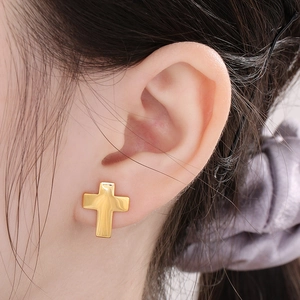 Close-up of 18K gold plated stainless steel cross stud earring on model ear