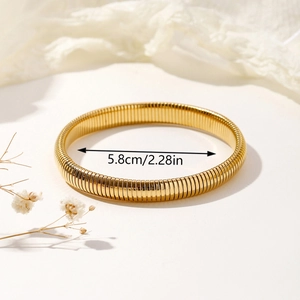 Elastic ribbed gold bangle with 5.8cm inner diameter on elegant white fabric background