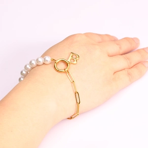 Detail of faux pearl and gold chain bracelet with letter B pendant on female wrist