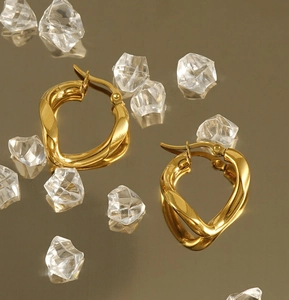 Detailed view of gold twisted hoop earrings on a reflective surface with ice cubes