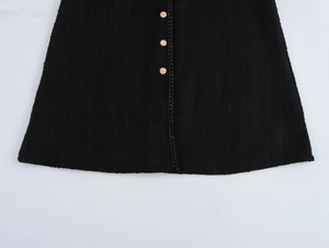 Dettaglio di un abito a trapezio in tweed nero con bottoni dorati e finiture ondulate
