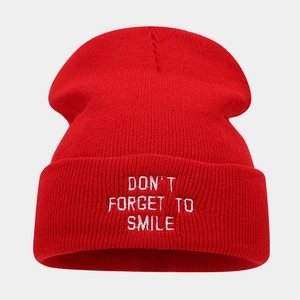 Detailed view of red knitted beanie featuring white 'Don't forget to smile' embroidery