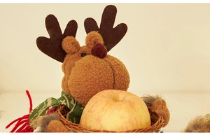 Nahaufnahme einer Weihnachtsrentier-Plüschpuppe mit kleinem Weidenkorb und Apfel.