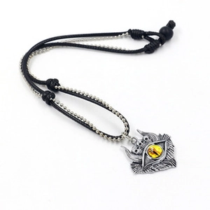 Close-up of gothic necklace with silver skull pendant, yellow eye, and black woven cord