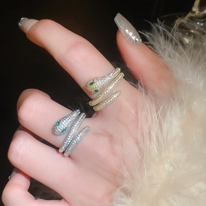 Close-up of gold and silver snake rings with white crystals and green stone eyes
