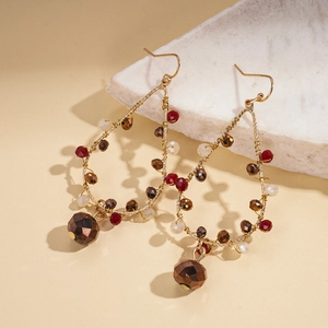 Boucles d'oreilles ethniques avec perles rouges et fil doré sur fond de marbre