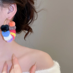 Close-up of a model wearing colorful plush pom-pom round hoop earrings in winter style