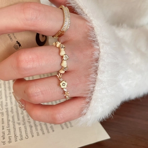 Ensemble de trois bagues dorées avec fleurs en nacre et accents de cœur sur les doigts