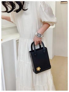 Detail der schwarzen EVA-Strandtasche mit gelbem Blumenanhänger und Armbanduhr
