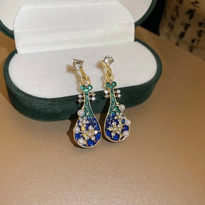 Macro shot of Pipa pearl earrings with blue enamel and rhinestones in a green velvet box
