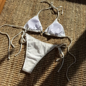 White textured bikini set with shell detail on woven straw mat under sunlight