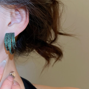 Close-up of a model wearing layered green zircon C-shaped hoop earrings in gold finish