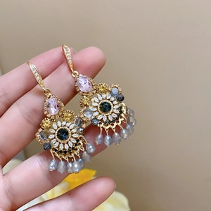 Détail de boucles d'oreilles fleurs avec cristaux roses et gris sur monture dorée