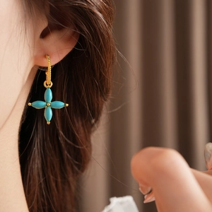 Close-up of a gold-plated four-leaf clover earring with green turquoise on a model ear