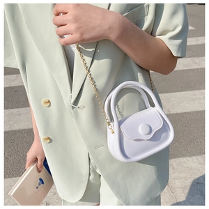 Minimalist white mini chain bag with glossy finish carried by a model on the street
