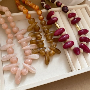 Close-up of resin beaded necklaces in pink, amber, and burgundy with golden accents