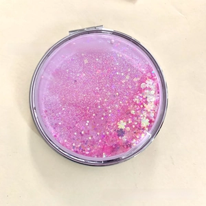 Detail shot of a round folding compact mirror featuring pink moving quicksand and sparkles