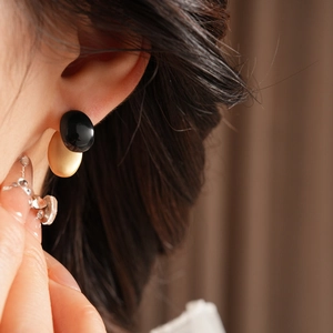 Close-up of stylish black and gold oval earrings worn by a model in soft lighting