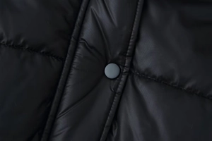 Detailed macro shot of matte black snap button and quilted windproof fabric on women's coat