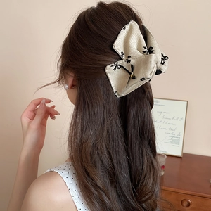 Detail of beige bow hair claw clip with black embroidery and gold pendant on hair