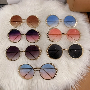 Round pearl-rimmed sunglasses with metal frames in various trendy colors on plush white background