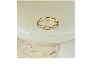 Macro shot of gold-plated chain link ring with sparkling zircons on a minimal base