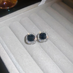 Detail of square dark gemstone stud earrings with a shimmering halo on velvet tray
