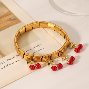 Detail of gold stainless steel modular bracelet with red cherry charms on vintage paper