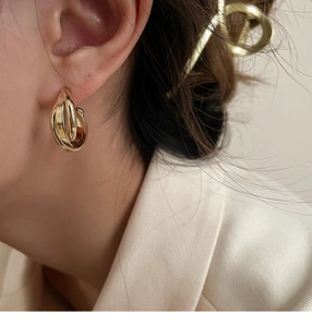 Gros plan de boucles d'oreilles clips dorées géométriques portées par un mannequin