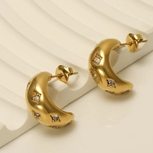 Détail de boucles d'oreilles dorées courbées avec zircons en étoile sur un socle en pierre