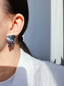 Close-up of geometric layered mirror finish silver earrings worn by a model in sunlight