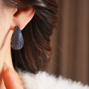 Macro view of teardrop earrings with deep blue crystals and dark plating on model