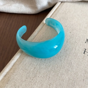 Macro shot of sky blue marble resin cuff bracelet on textured book with warm lighting